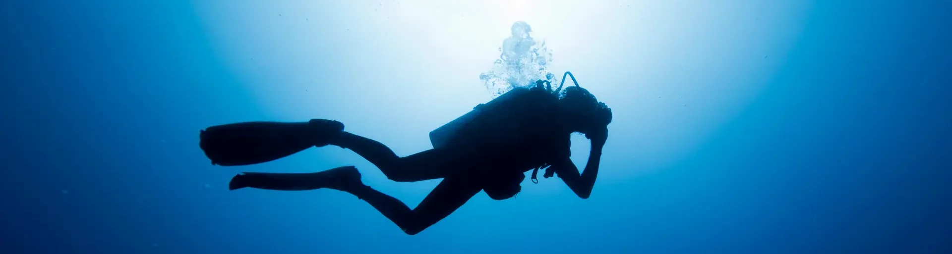 Image horizontale large représentant une plongeur loisir en vue de coté dans une ambiance sombre